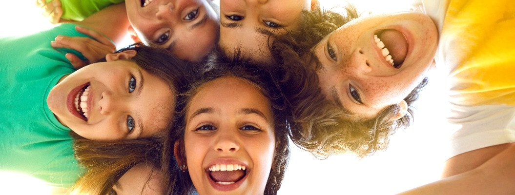Bunch of cheerful joyful cute little children playing together and having fun. Group portrait of happy kids huddling, looking down at camera and smiling. Low angle, view from below. Friendship concept
