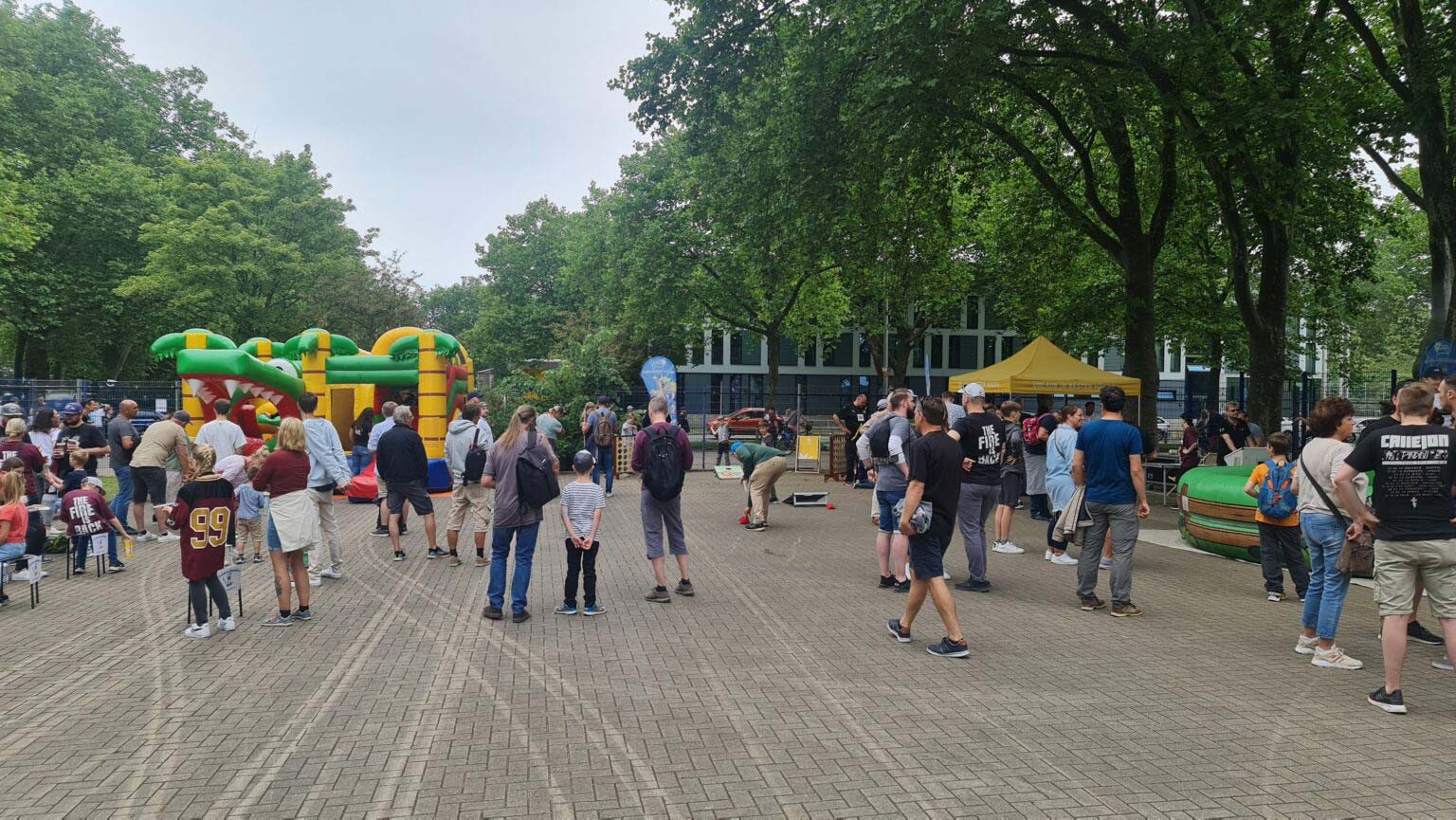 Menschenmenge auf einer Veranstaltung in einem Park mit Hüpfburgen, sommerlich gekleidet.