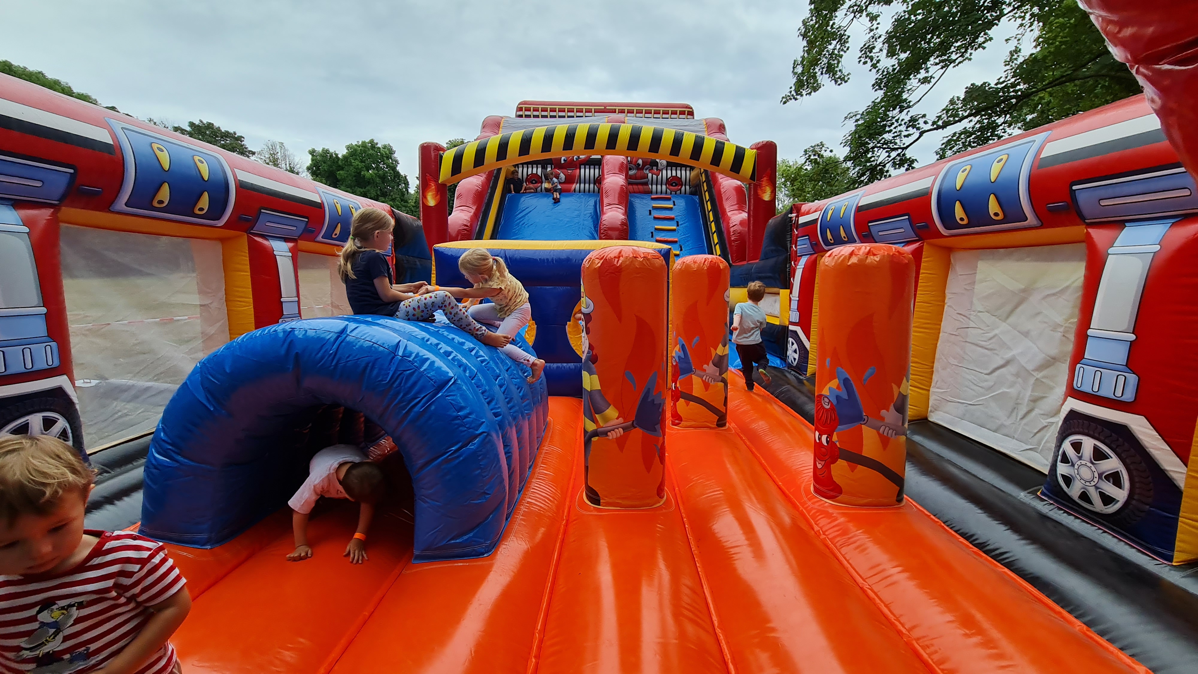 Kinder spielen fröhlich auf einer bunten Hüpfburg mit Rutschbahn und Tunnel.