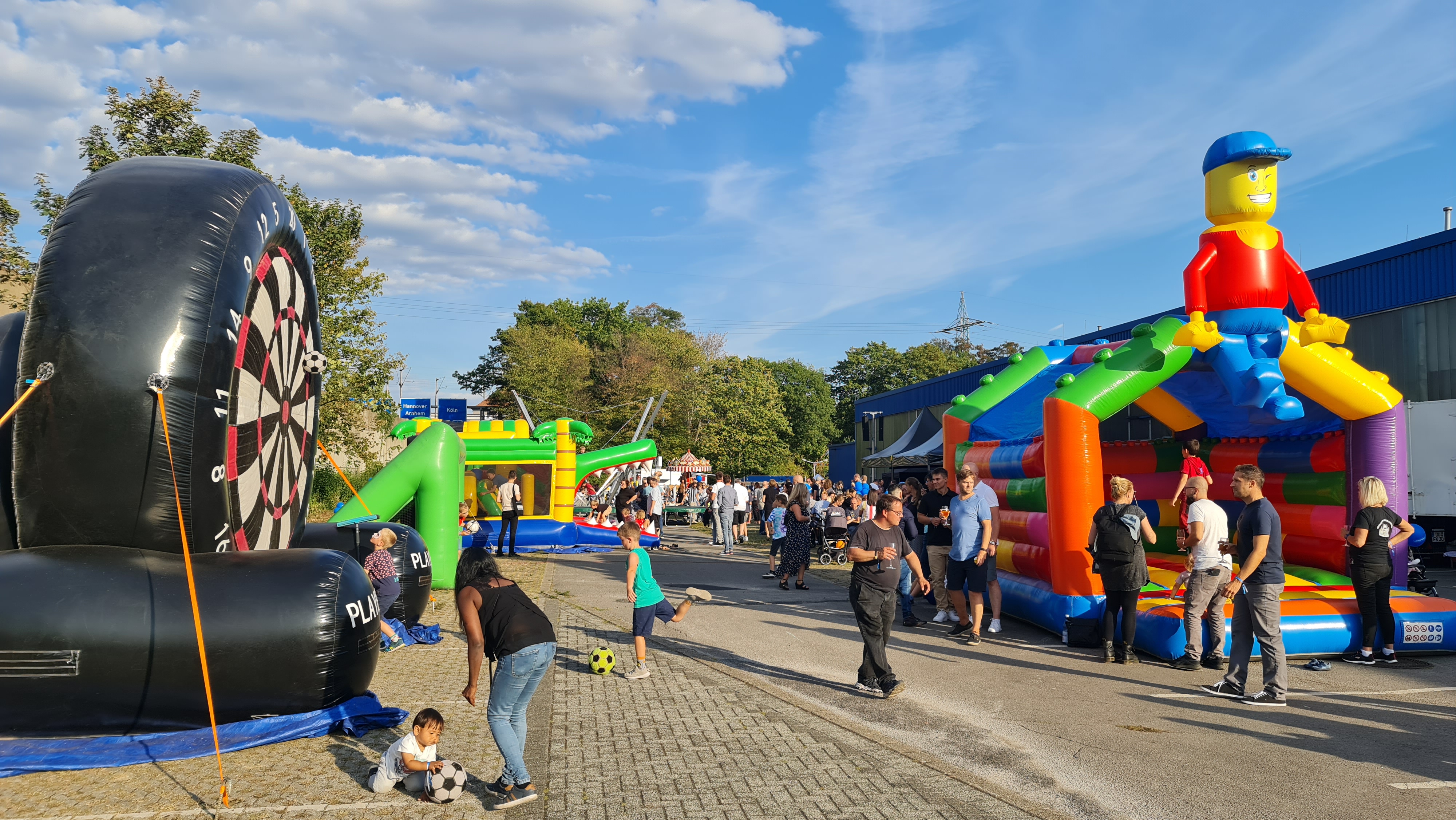 Menschen genießen eine sonnige Outdoor-Event mit bunten Hüpfburgen und Spielgeräten.