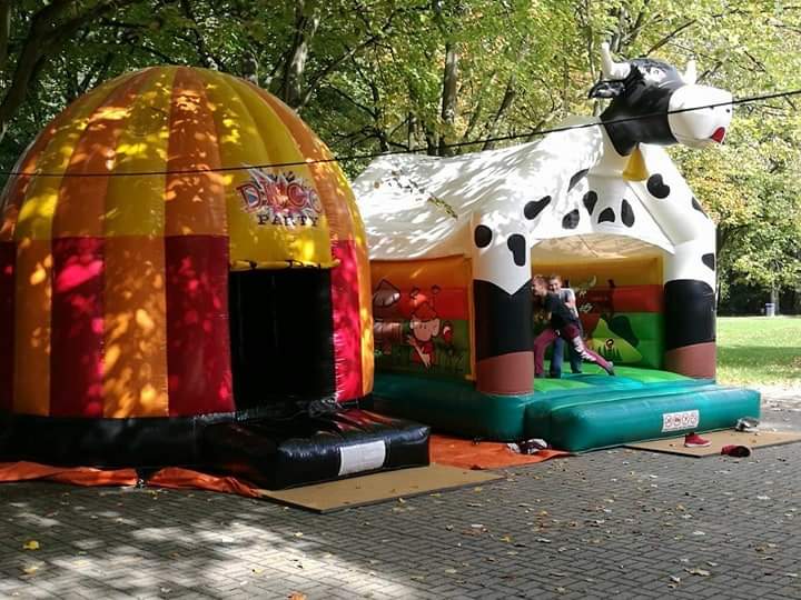 Zwei Kinder spielen auf einer Kuh-Hüpfburg im Park, umgeben von grünen Blättern und Sonnenschein.