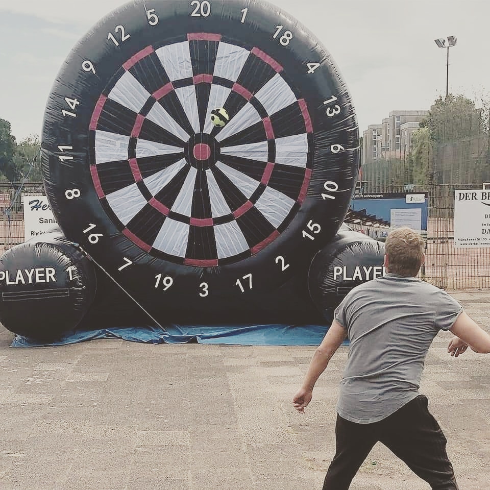 Eine Person in einem grauen Shirt wirft auf eine riesige aufblasbare Fußballdartscheibe.