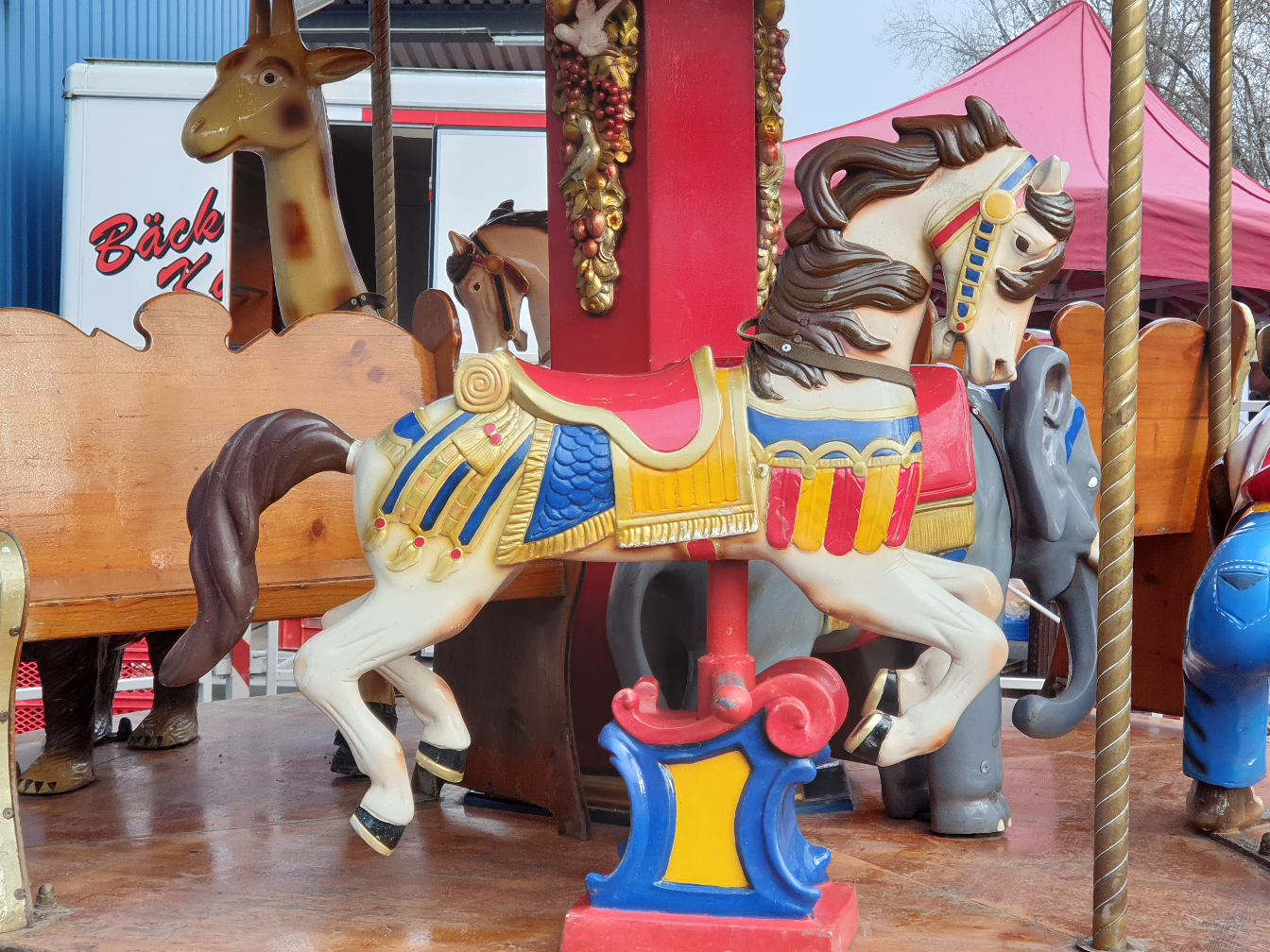 Ein buntes Karussellpferd mit fröhlichem Ausdruck, umgeben von anderen Tierfiguren.