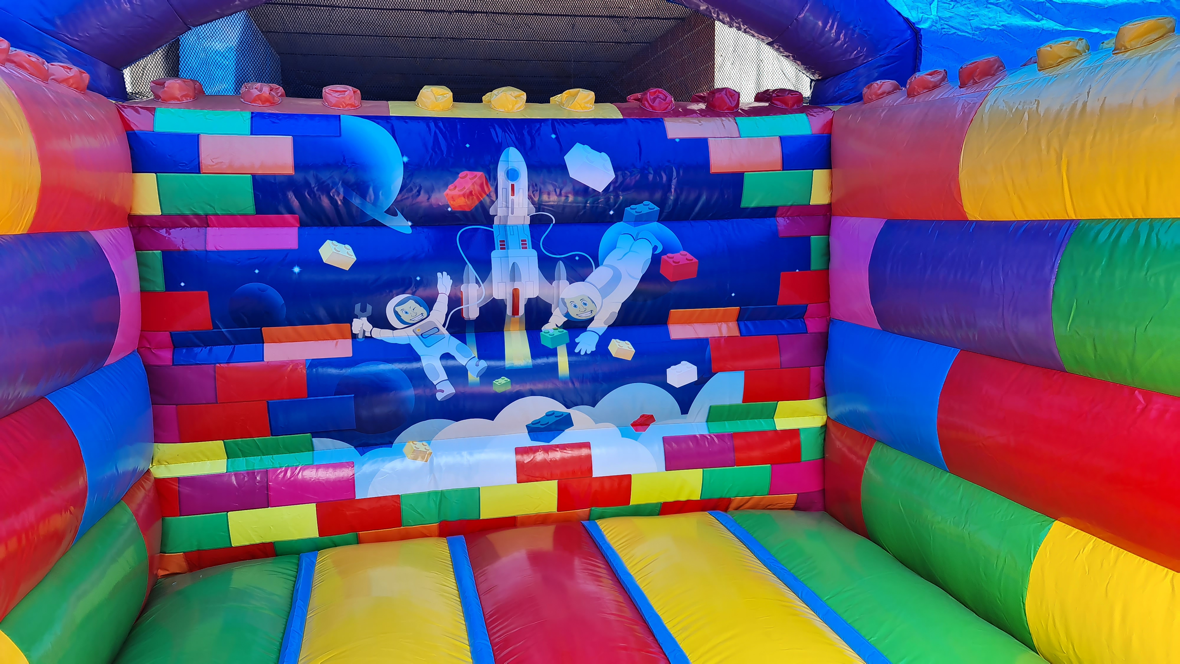 Bunte Hüpfburg mit Astronautenmuster und planetarischem Design, keine Personen sichtbar.