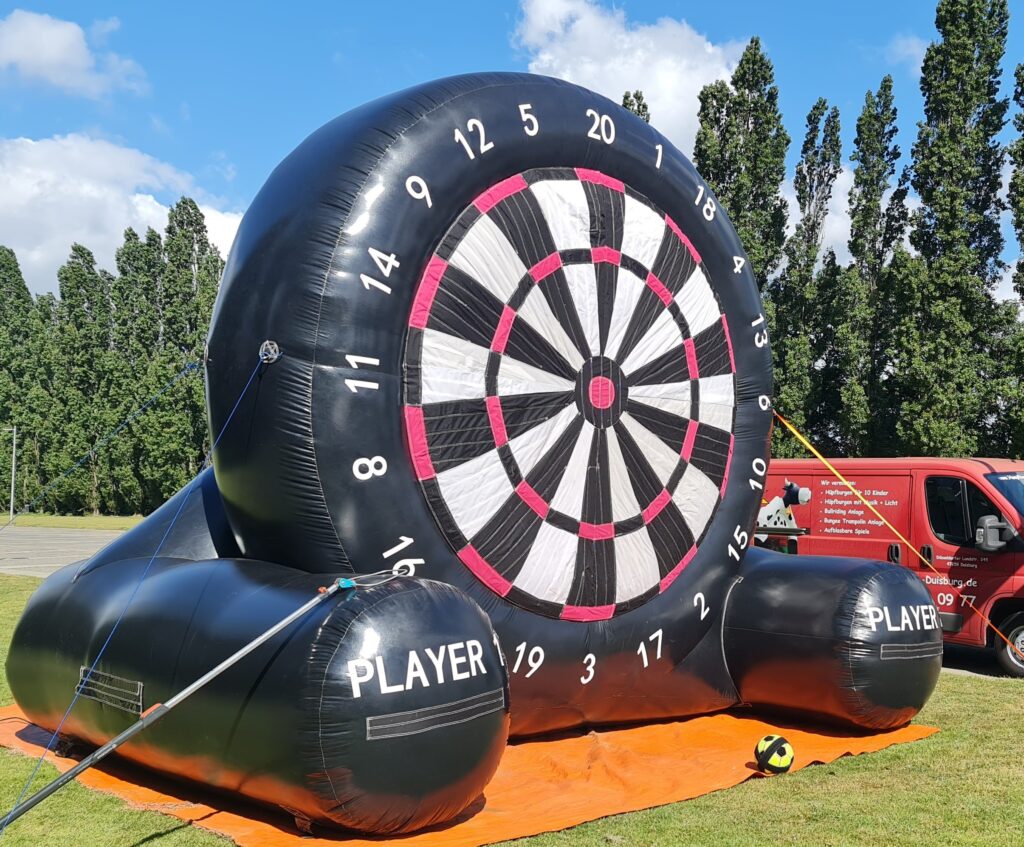 Aufblasbare Dartscheibe, schwarz-weiß mit rosafarbenen Akzenten im Freien auf einer Wiese.
