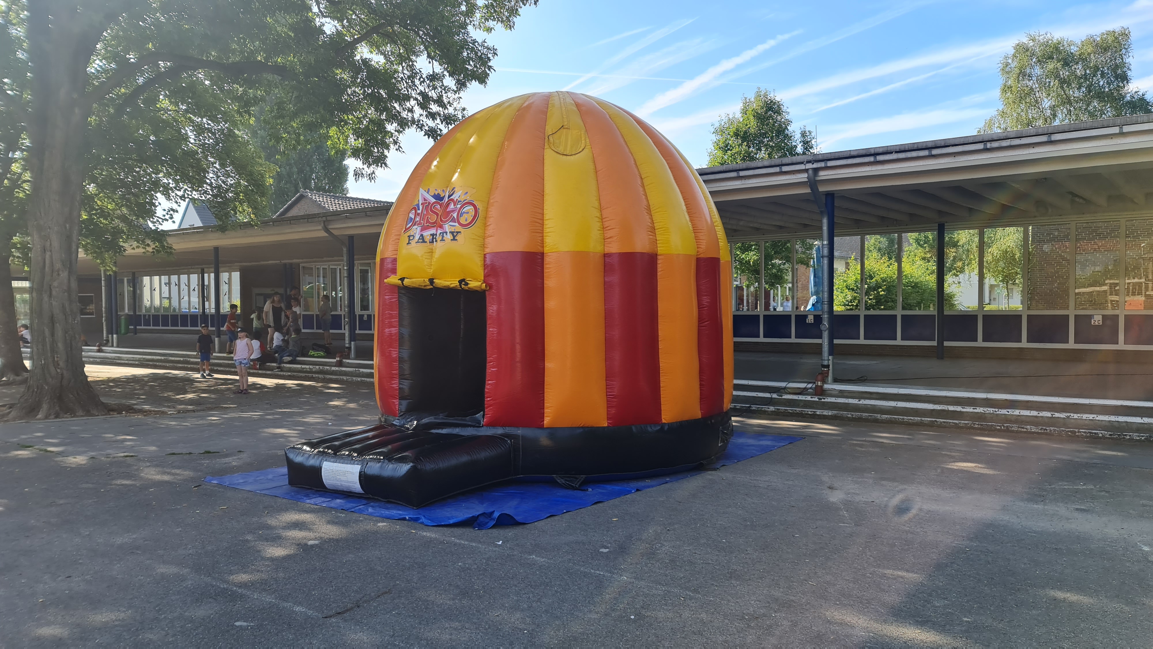 Eine große, orange-rot gestreifte Hüpfburg im Freien auf einem blauen Untergrund.