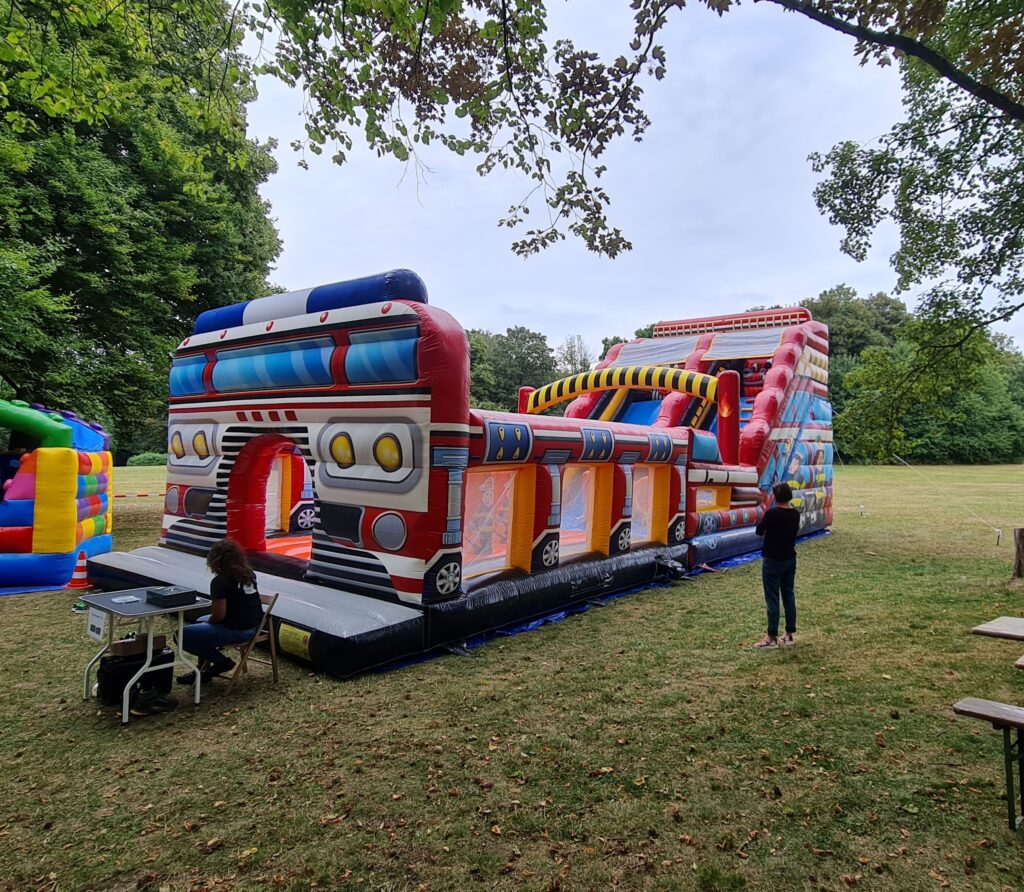 Eine bunte Hüpfburg mit Spielautomatenthema im Park, umgeben von grasbewachsenen Flächen.