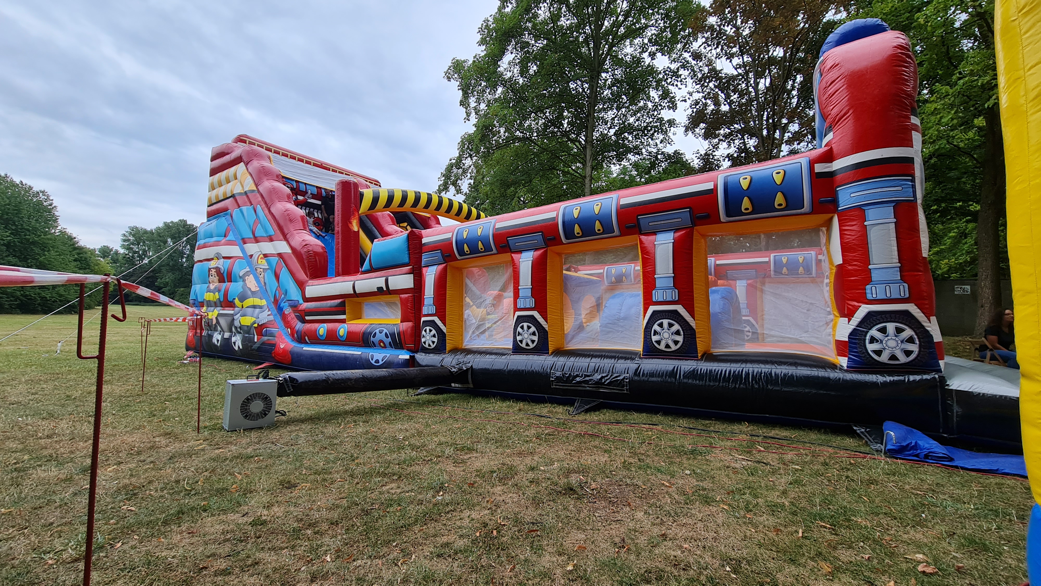 Eine bunte, aufblasbare Hüpfburg auf einer Wiese vor Bäumen.
