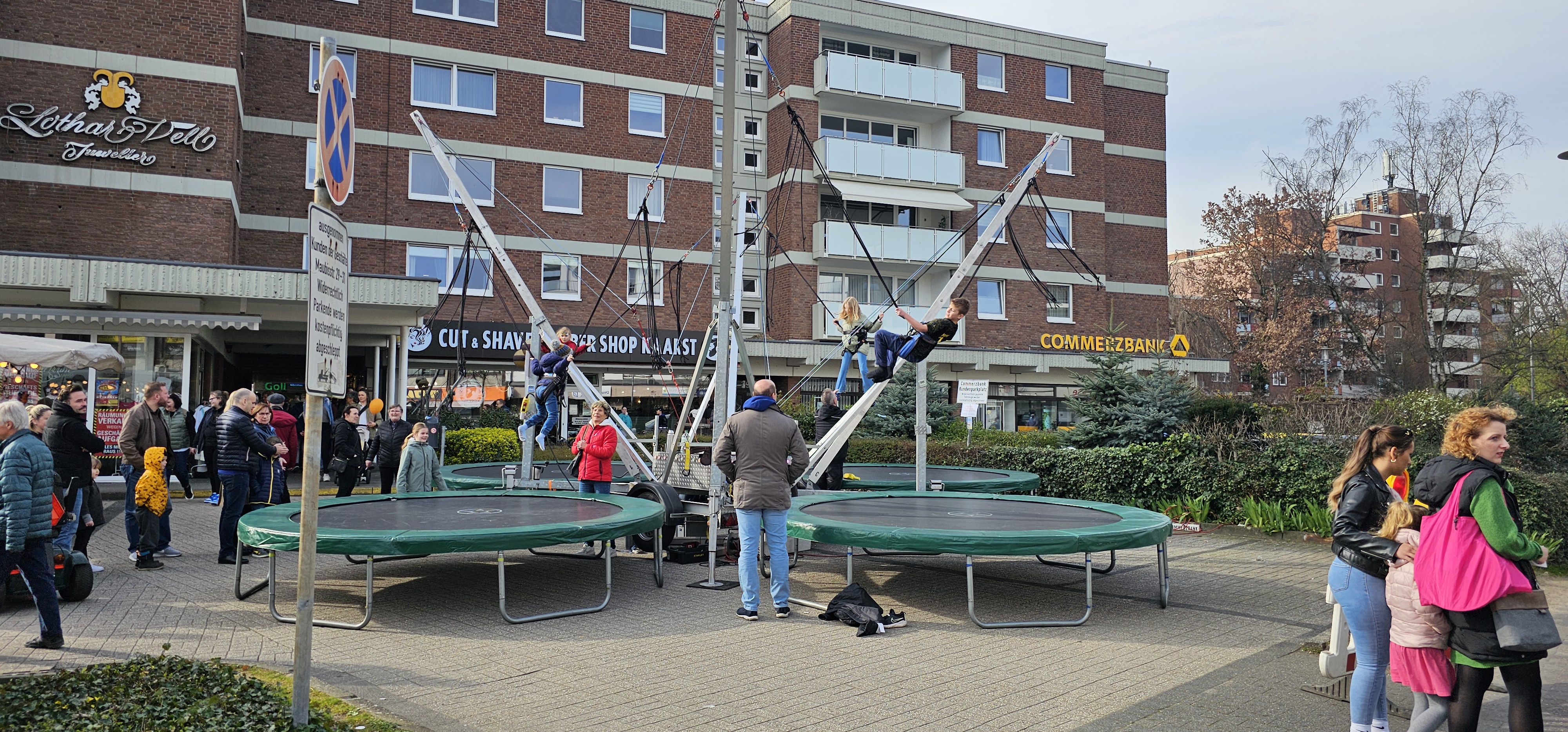 Eine Gruppe von Personen genießt Trampolinspringen auf einem Platz, umgeben von Gebäuden.