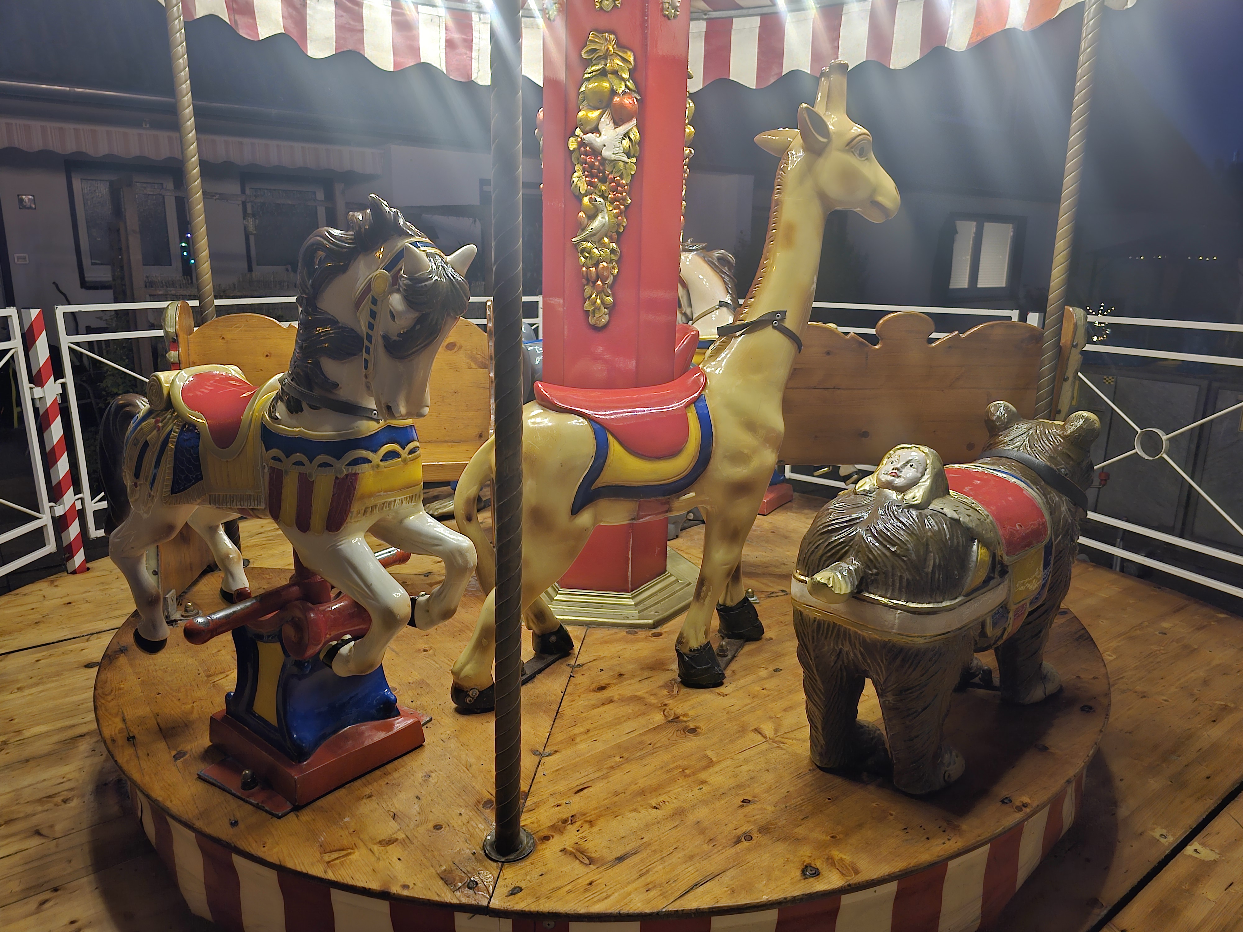 Ein nostalgisches Karussell mit Tierfiguren: Pferd, Giraffe, Bär und Schaf, beleuchtet, bunt bemalt.