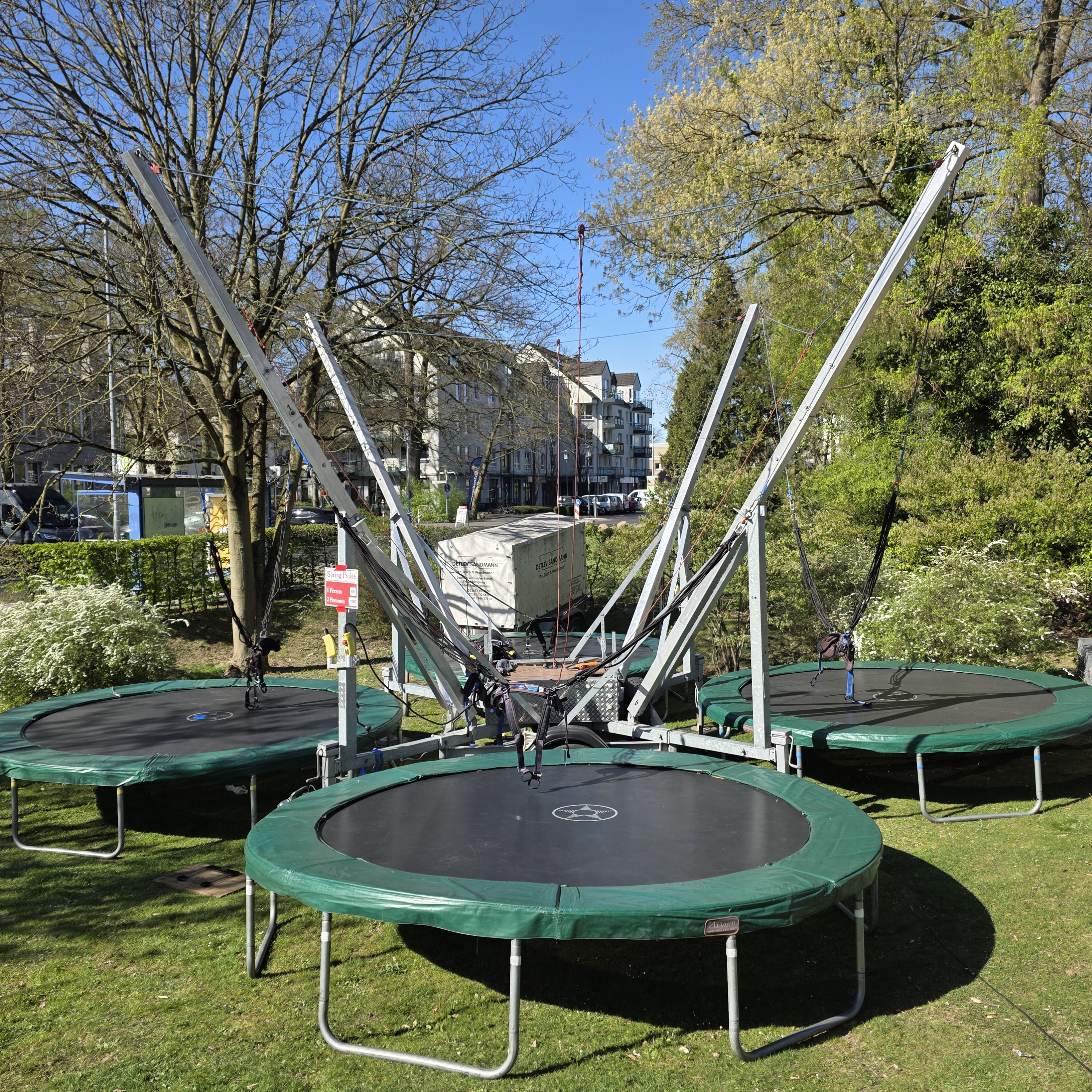 Grüner Trampolinpark mit blühenden Bäumen im Hintergrund an einem sonnigen Frühlingstag.