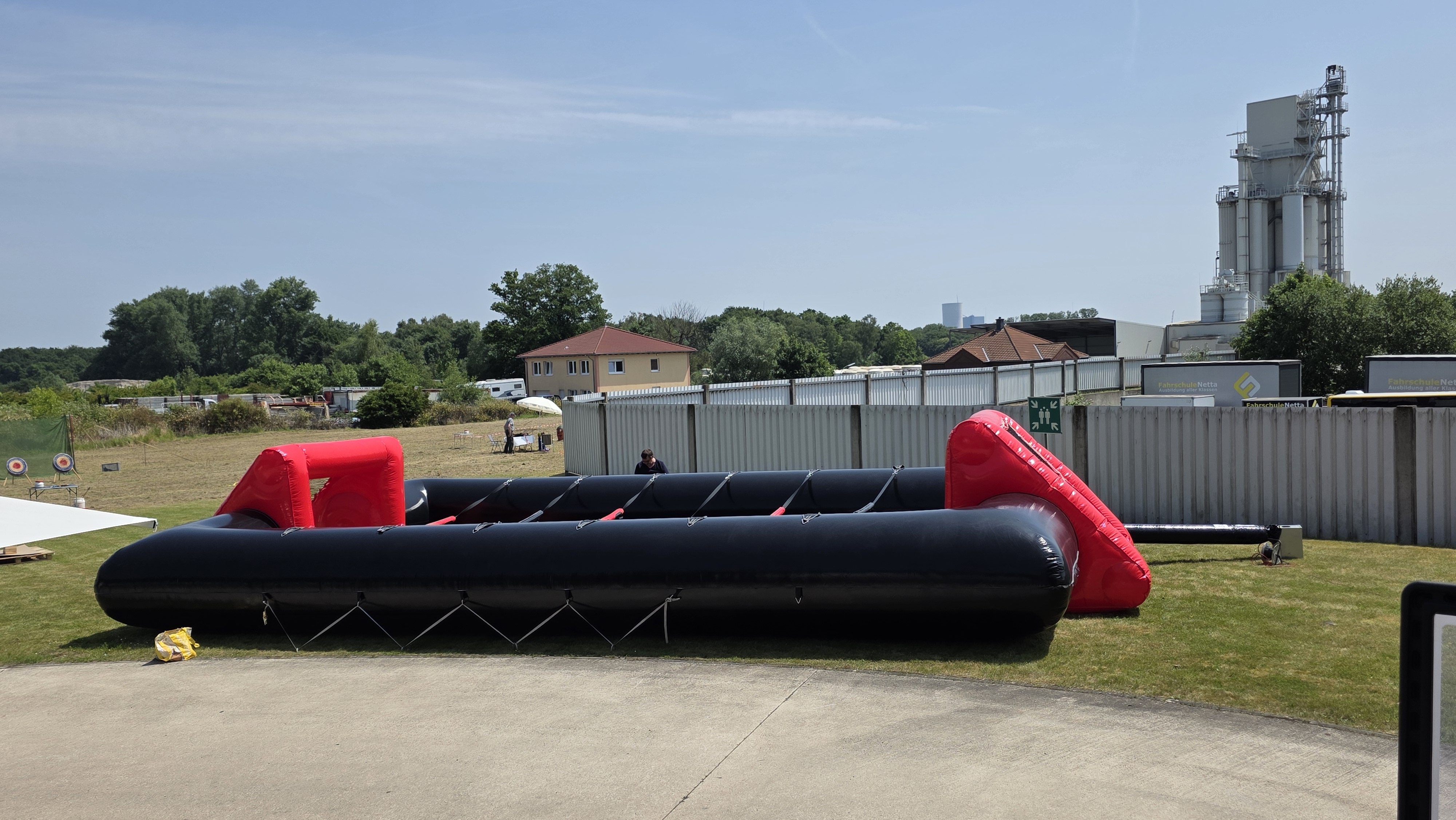 Aufblasbarer Fußballplatz im Freien, rot und schwarz, auf Rasen vor Industriegebäuden.
