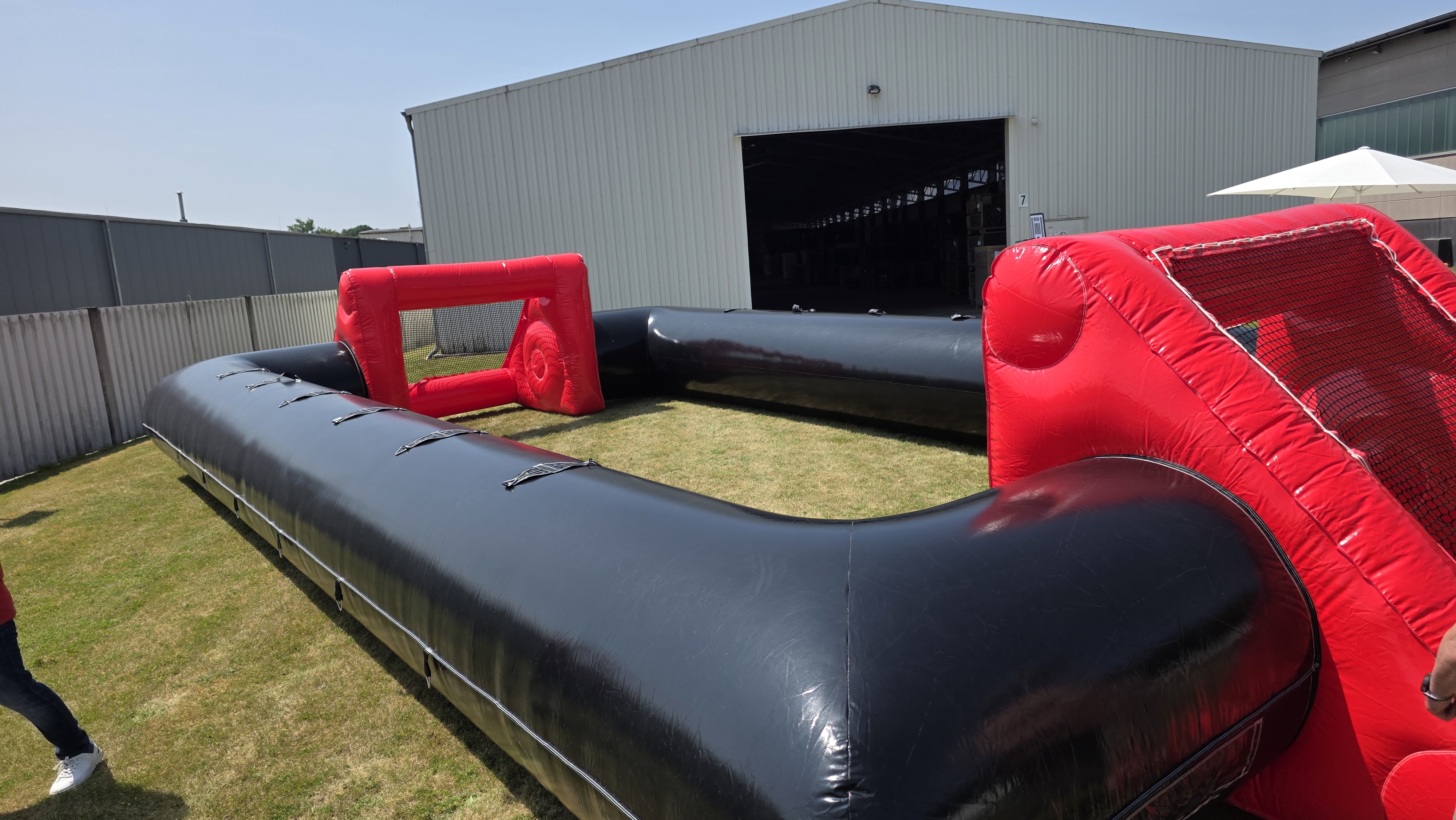 Aufblasbares Spielfeld in Rot und Schwarz mit Toren auf grünem Rasen vor einer Halle.