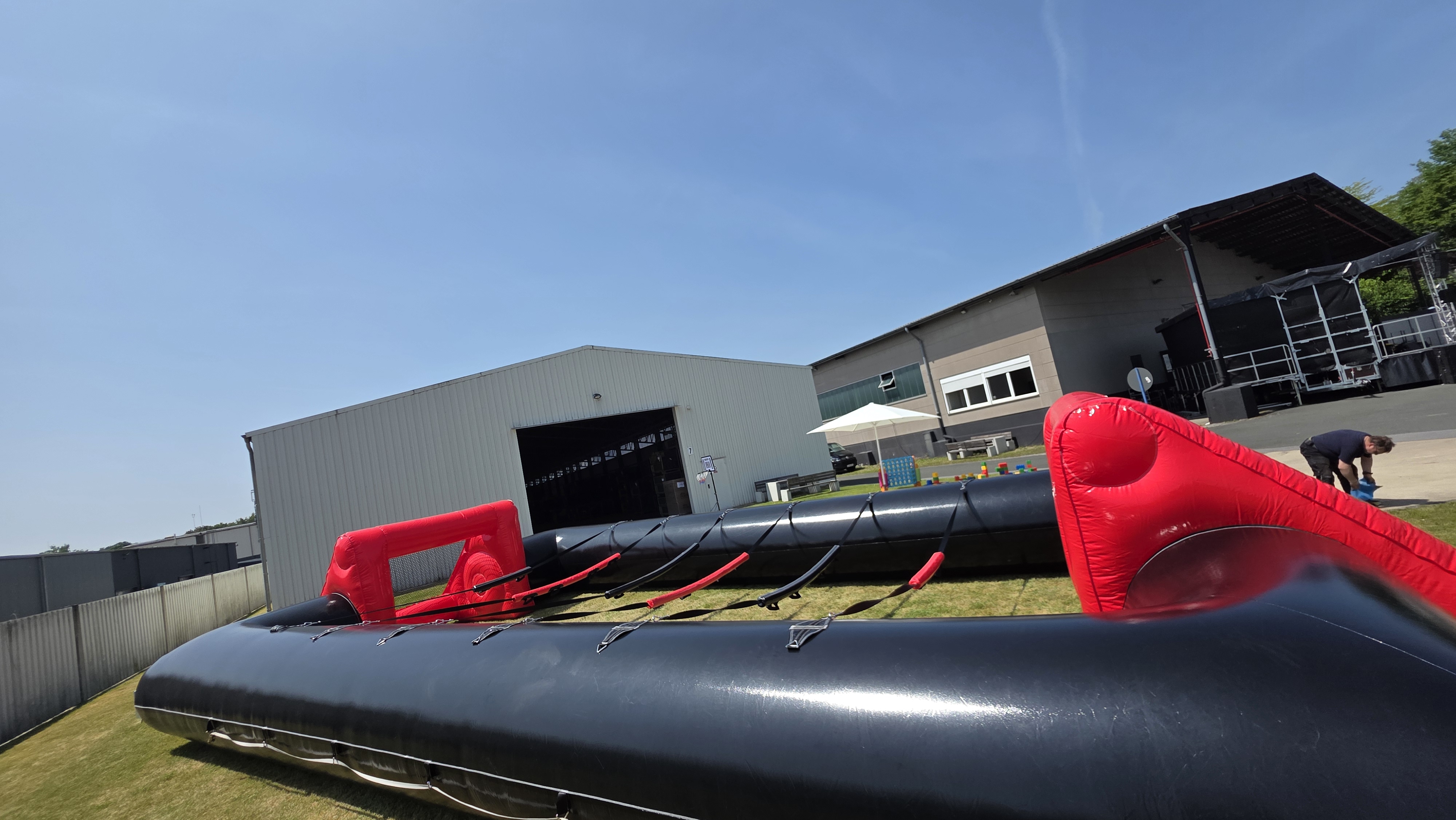 Aufblasbare Spielfläche mit roten und schwarzen Elementen auf Gras vor grauen Gebäuden.