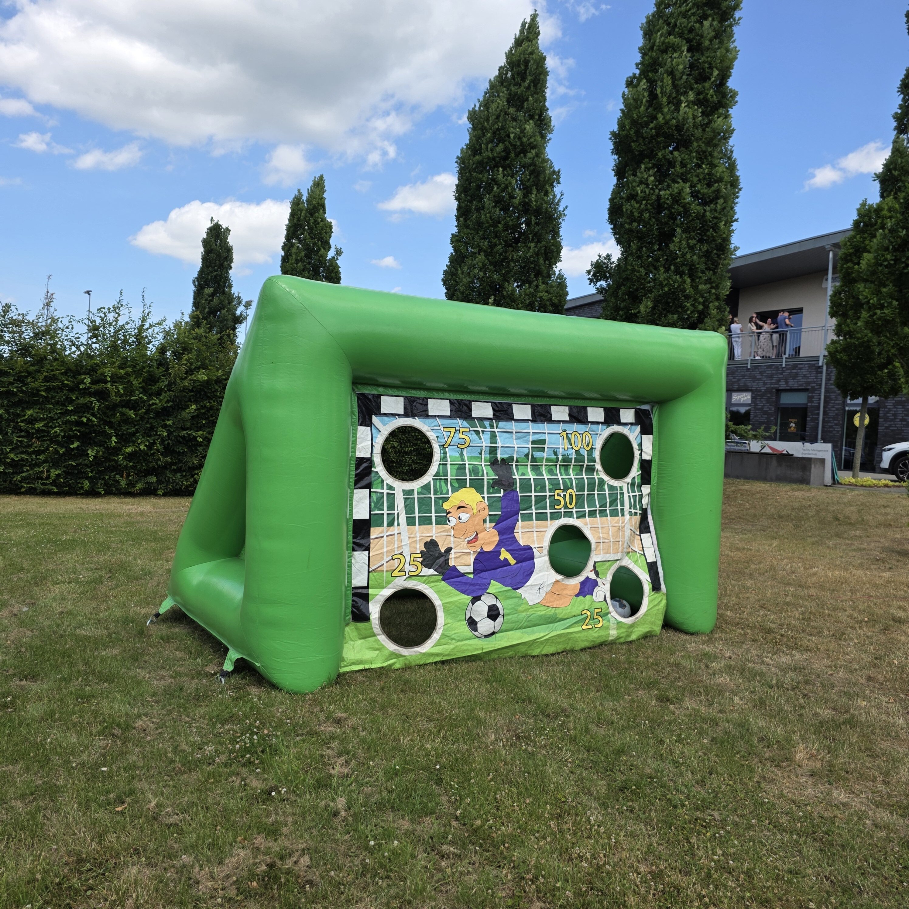 Aufblasbares grünes Fußballtor mit Lochzielen im Freien, bunte Comic-Grafik, sonniges Wetter.