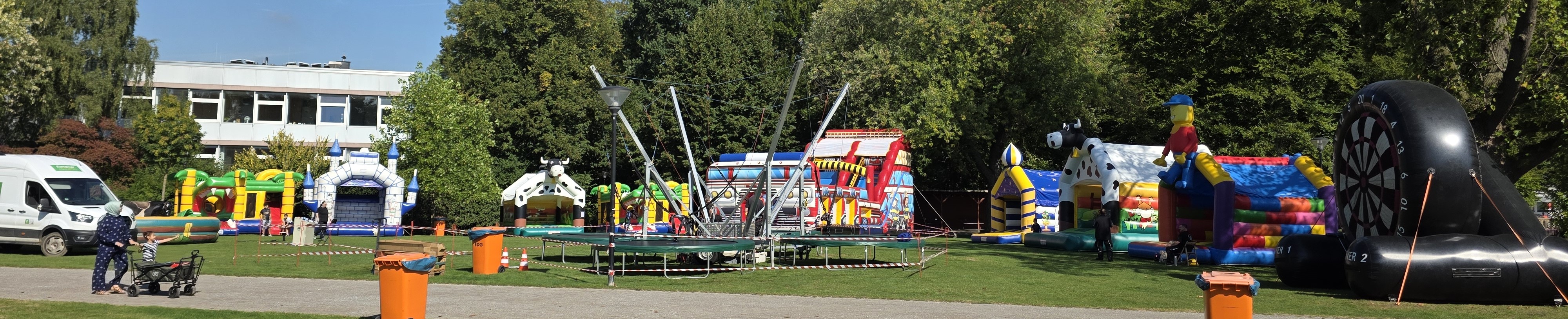 Ein Park mit bunten Hüpfburgen und Trampolinen, umgeben von Bäumen im Sonnenschein